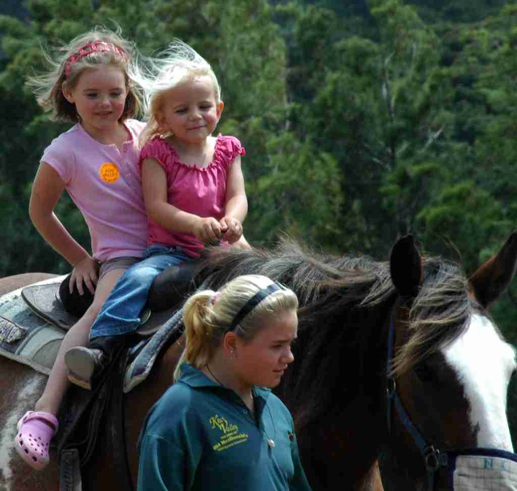 two young girls riding a horse with a woman leading it
